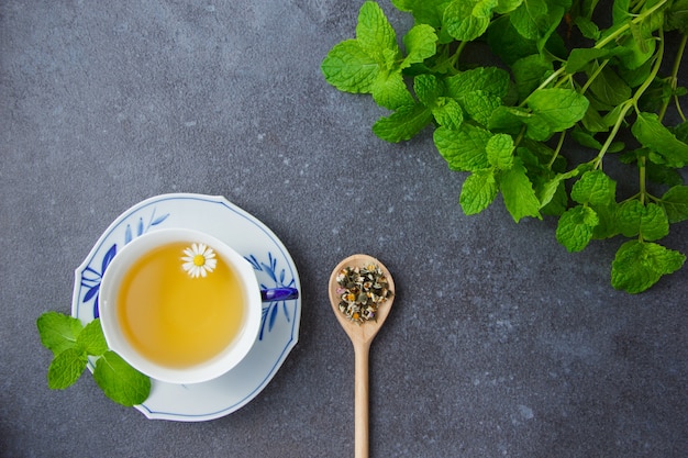 Top view a cup of chamomile tea with mint leaves and chamomile herbs in spoon.