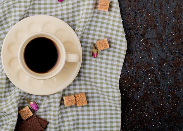Вид сверху чашки кофе и коричневого сахара, разбросанных на клетчатой скатерти с копией пространства