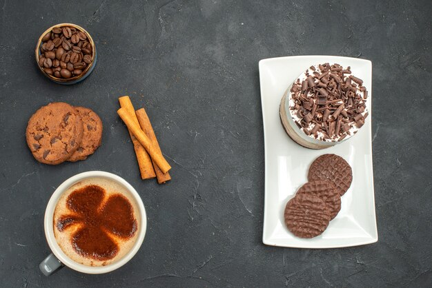 Top view a cup of coffee cake and biscuits on white plate on dark isolated background