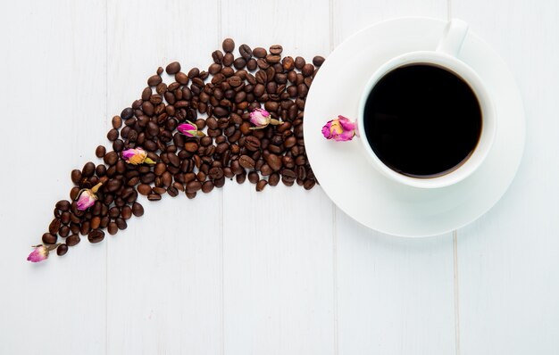 Top view of a cup of coffee and coffee beans scattered on white background