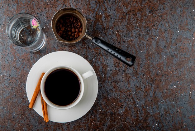 Top view of a cup of coffee and a coffee pot with beans on black background with copy space