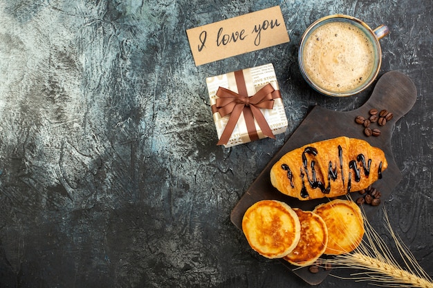 Top view of a cup of coffee and fresh delicious breakfast beautiful gift box pancakes croisasant on dark background