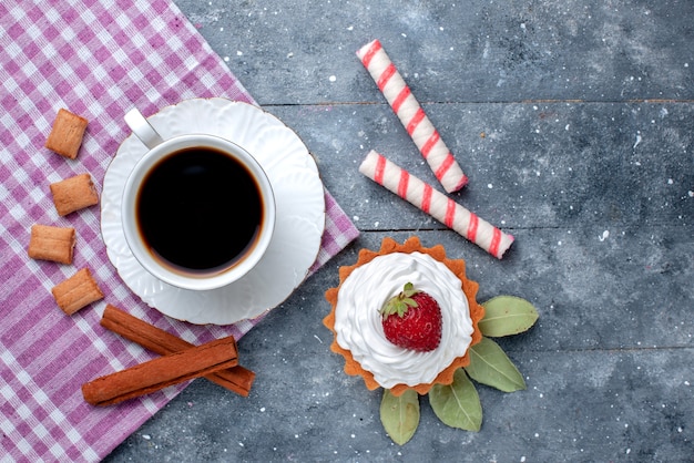 Вид сверху на чашку горячего и крепкого кофе вместе с тортом и корицей на сером столе, сладкий напиток из кофейных конфет