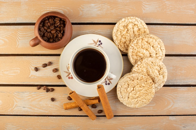 A top view cup of coffee hot and strong with fresh brown coffee seeds cinnamon and crackers on the cream rustic desk coffee seed drink photo grain