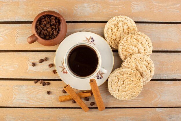 A top view cup of coffee hot and strong with fresh brown coffee seeds cinnamon and crackers on the cream rustic desk coffee seed drink photo grain