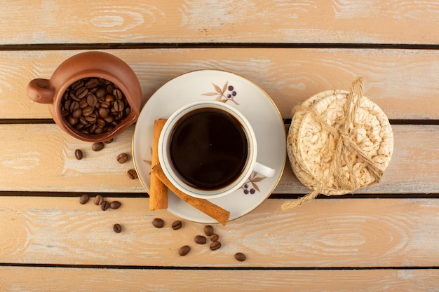 A top view cup of coffee hot and strong with fresh brown coffee seeds cinnamon and crackers on the cream rustic desk coffee seed drink photo grain