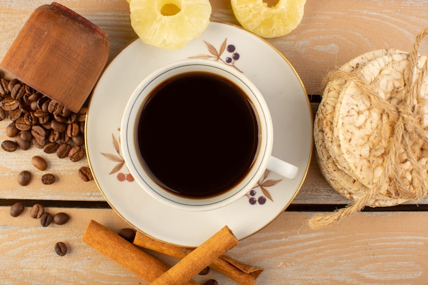 A top view cup of coffee hot and strong with fresh brown coffee seeds cinnamon and crackers on the cream rustic desk coffee seed drink photo grain