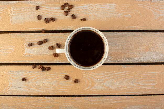 クリームの素朴なデスクのコーヒーシードの飲み物の写真の穀物に新鮮な茶色のコーヒーの種子とホットで強いコーヒーのトップビューカップ