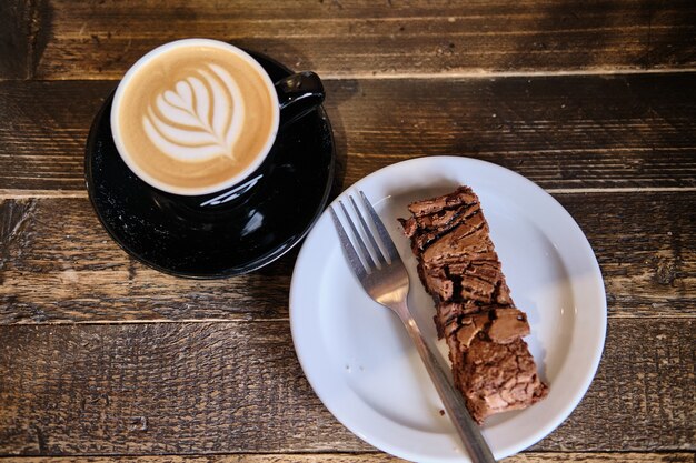 Top view of a cup of coffee and plate of chocolate cake on a wooden table