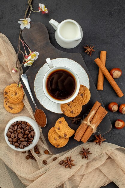 Top view cup of coffee star anises cookies spoon on wood board coffee beans in bowl milk bowl on dark surface