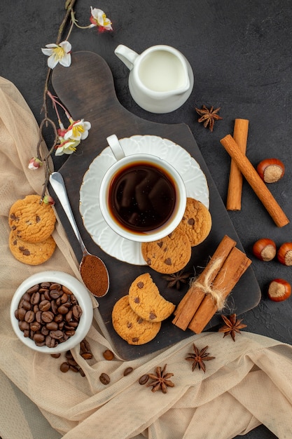 Top view cup of coffee star anises cookies spoon on wood board coffee beans in bowl milk bowl on dark surface