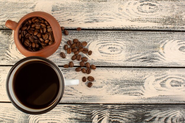 A top view cup of coffee with brown coffee seeds on the grey rustic desk drink coffee color