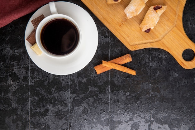 Top view of  a cup of coffee with chocolate cinnamon sticks and flour cookies on black background