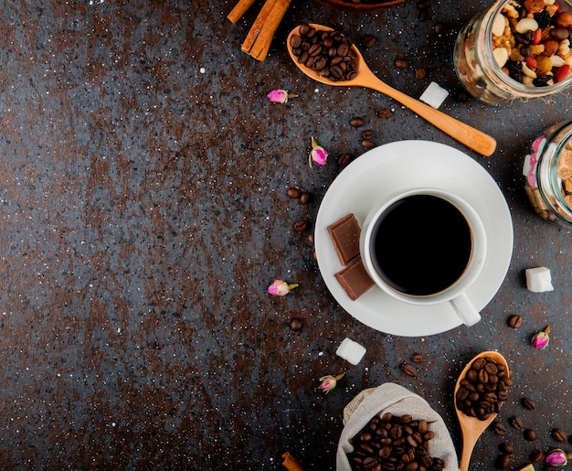 Top view of a cup of coffee with chocolate and a wooden spoon with coffee beans on black background