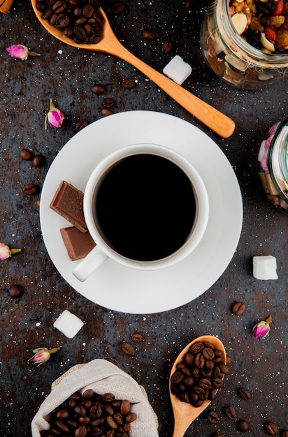 Top view of a cup of coffee with chocolate and a wooden spoon with coffee beans on black background