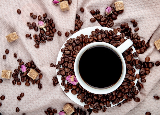 Top view of a cup of coffee with coffee beans brown sugar cubes and tea rose buds