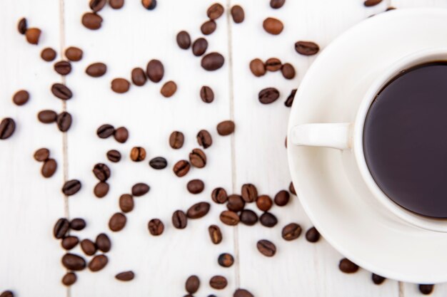 Top view of a cup of coffee with coffee beans isolated on a white wooden background