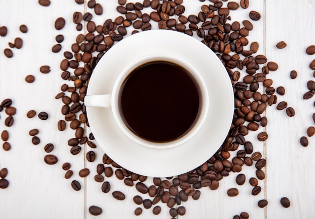 白い木製の背景に分離されたコーヒー豆とコーヒーのカップの上から見る