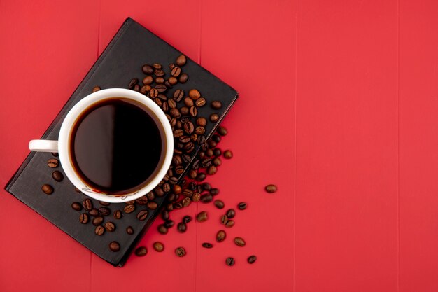 Top view of a cup of coffee with coffee beans on a red background with copy space