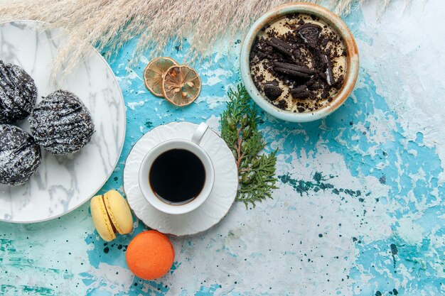 Вид сверху чашка кофе с французскими макаронами и шоколадными пирожными на голубом фоне, выпечка торта, бисквит, сладкий шоколад, сахарный цвет