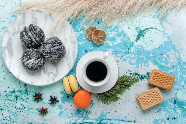 Top view cup of coffee with french macarons waffles and chocolate cakes on blue surface cake bake biscuit sweet chocolate sugar color