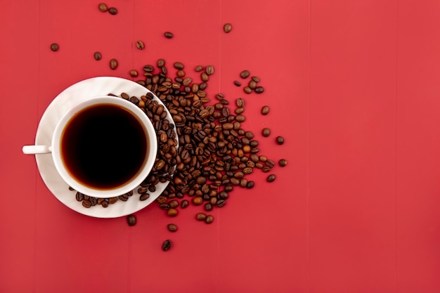 복사 공간이 빨간색 배경에 고립 된 신선한 볶은 커피 원두와 커피 한 잔의 상위 뷰