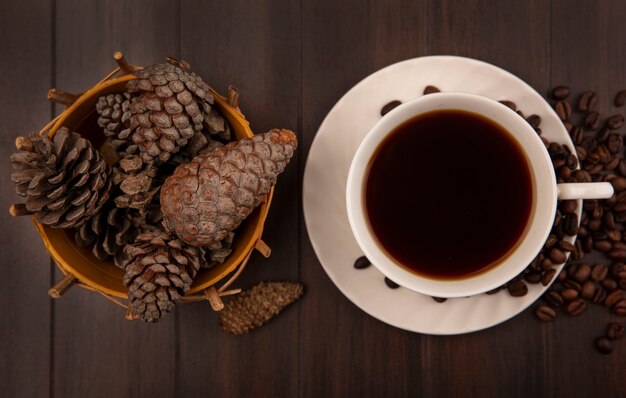 Top view of a cup of coffee with pine cones on a bucket with coffee beans isolated on a wooden surface