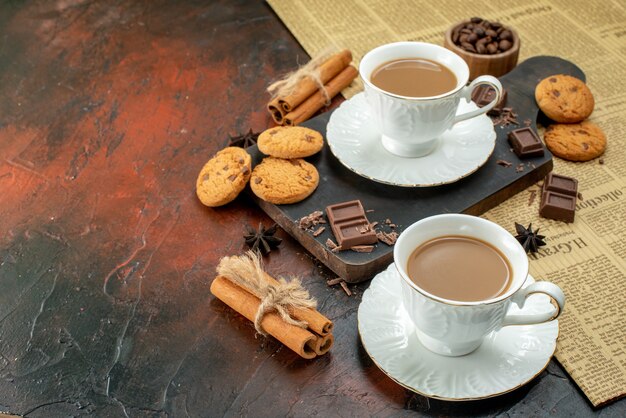 Top view of cup of coffee on wooden cutting board on an old newspaper cookies cinnamon limes chocolate bars on the left side