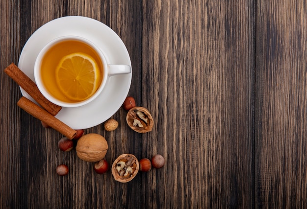 Top view of cup of hot toddy with cinnamon on saucer and nuts walnuts on wooden background with copy space