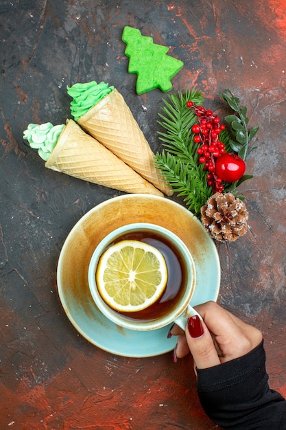 Бесплатное фото Вид сверху чашка чая со вкусом лимона в женской руке мороженое из ветки рождественского дерева на темно-красном столе