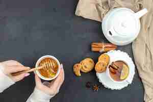 Бесплатное фото Вид сверху чашка чая с медом и печеньем на темном фоне обед церемония еды завтрак пищевой цвет лимонное печенье женщина