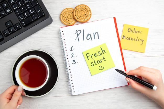 白い背景の日計画甘い学校レジームコピーブックキーボードにメモ帳を書いた計画スケジュールとお茶のトップビューカップ