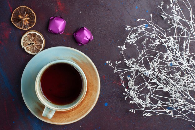 Top view of cup of tea along with chocolate candies on the dark surface