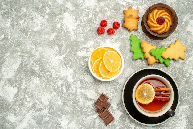 Вид сверху чашка чая, печенье и ломтики лимона в мисках, рождественское печенье на серой поверхности, свободное пространство