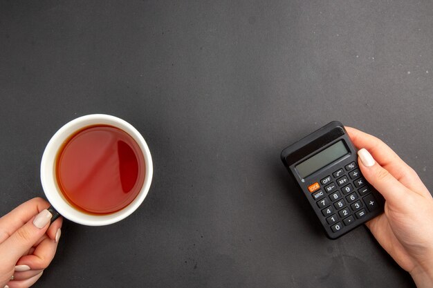 Top view cup of tea and calculator in female hands on dark table