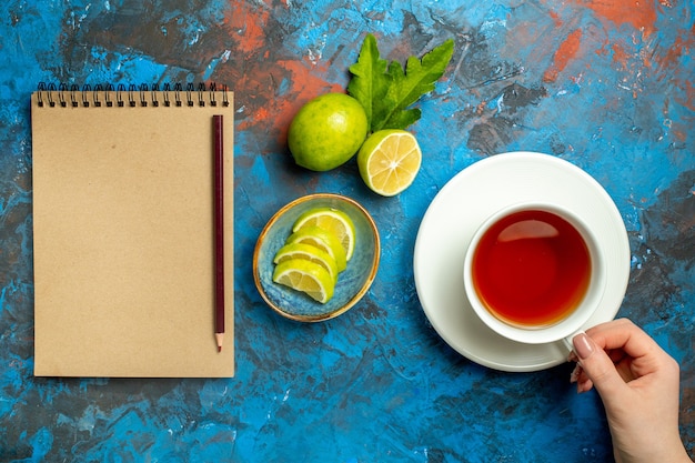 上面図青赤の表面上のノートにレモンの鉛筆を捕まえる女性の手スライスのお茶のカップ