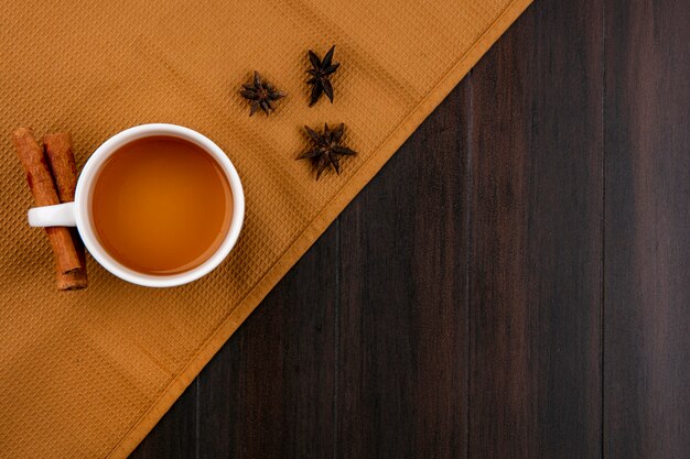 Top view of cup of tea and cinnamon on a brown towel on a wooden surface