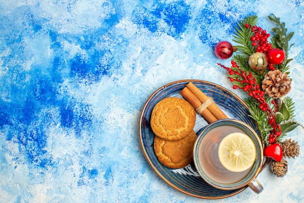 Top view cup of tea cinnamon sticks biscuits on saucer on blue table