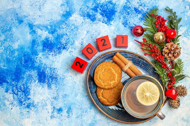 Top view cup of tea cinnamon sticks biscuits on saucer wood blocks xmas tre branches on blue table free space