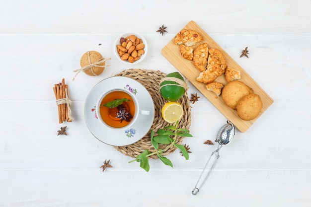 Top view a cup of tea, citrus fruits and mint leaves on round placemat with cookies on a cutting board