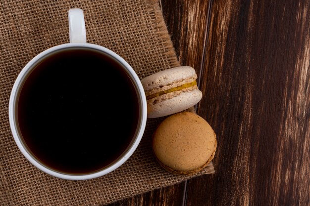 Top view of cup of tea and cookie sandwiches on sackloth and wooden background with copy space