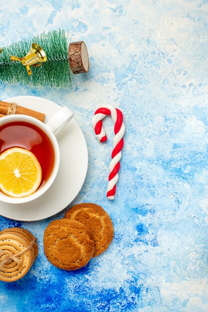 青いテーブルの上のロープの小さなクリスマスツリーとキャンディーで縛られたお茶のクッキーのトップビューカップ