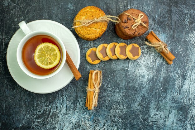 Foto gratuita vista dall'alto tazza di tè aromatizzata da biscotti al limone legati con bastoncini di cannella in corda su sfondo grigio