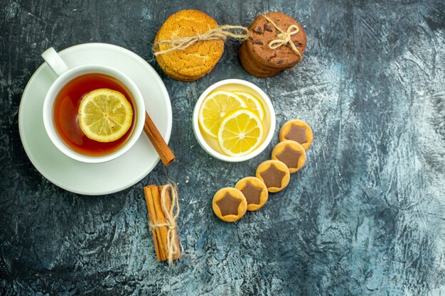 Top view cup of tea flavored by lemon and cinnamon biscuits with chocolate cookies tied with rope cinnamon sticks on grey background