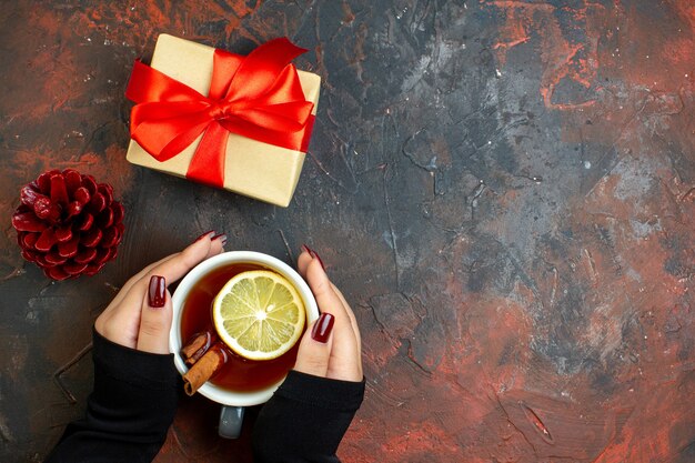 Top view cup of tea flavored by lemon and cinnamon in female hand xmas gift on dark red table free place