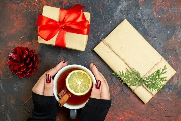 Top view cup of tea flavored by lemon and cinnamon in female hand xmas gifts on dark red table