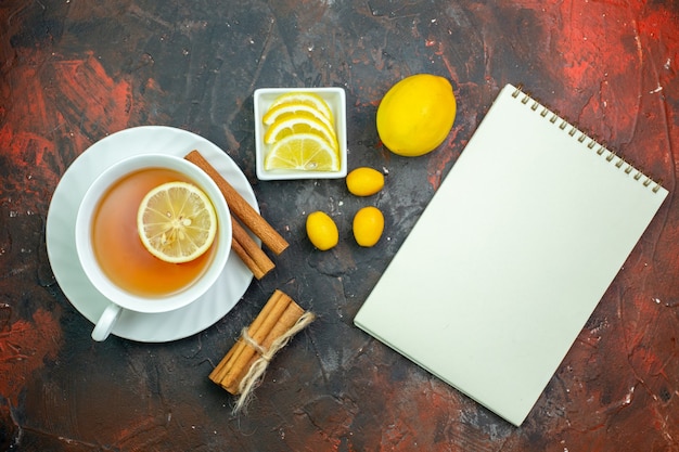 濃い赤の背景に小さなボウルシナモンメモ帳でレモンcumcuatレモンスライスで味付けされたお茶のトップビューカップ