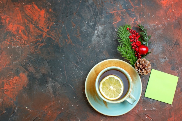 濃い赤のテーブルの無料の場所にレモンの付箋クリスマスツリーの枝で味付けされたお茶のトップビューカップ