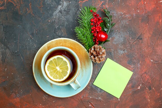 濃い赤のテーブルにレモンの付箋クリスマスツリーの枝で味付けされたお茶のトップビューカップ