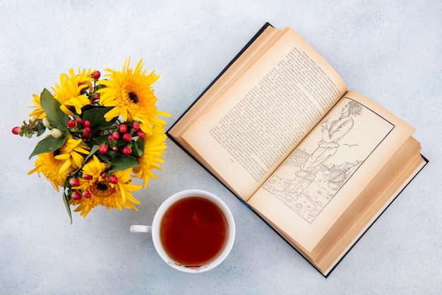 Top view of cup of tea and flowers with open book on white